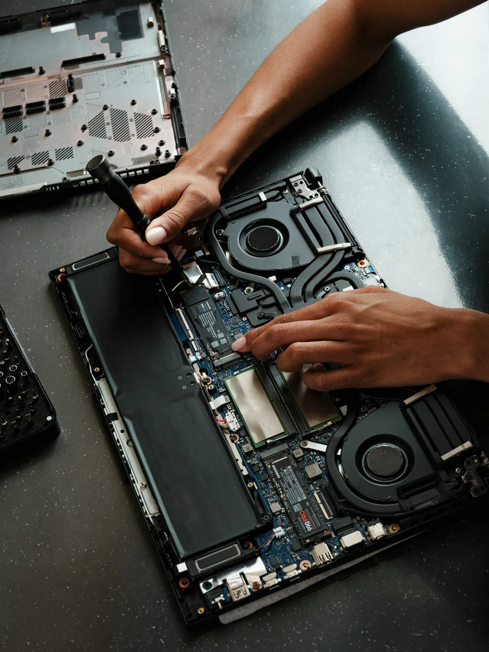 Manos reparando una laptop abierta con un destornillador